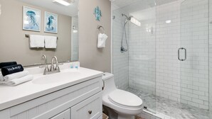 Un baño con un lavamanos blanco, un inodoro, una ducha con mampara de vidrio y dos cuadros en la pared.