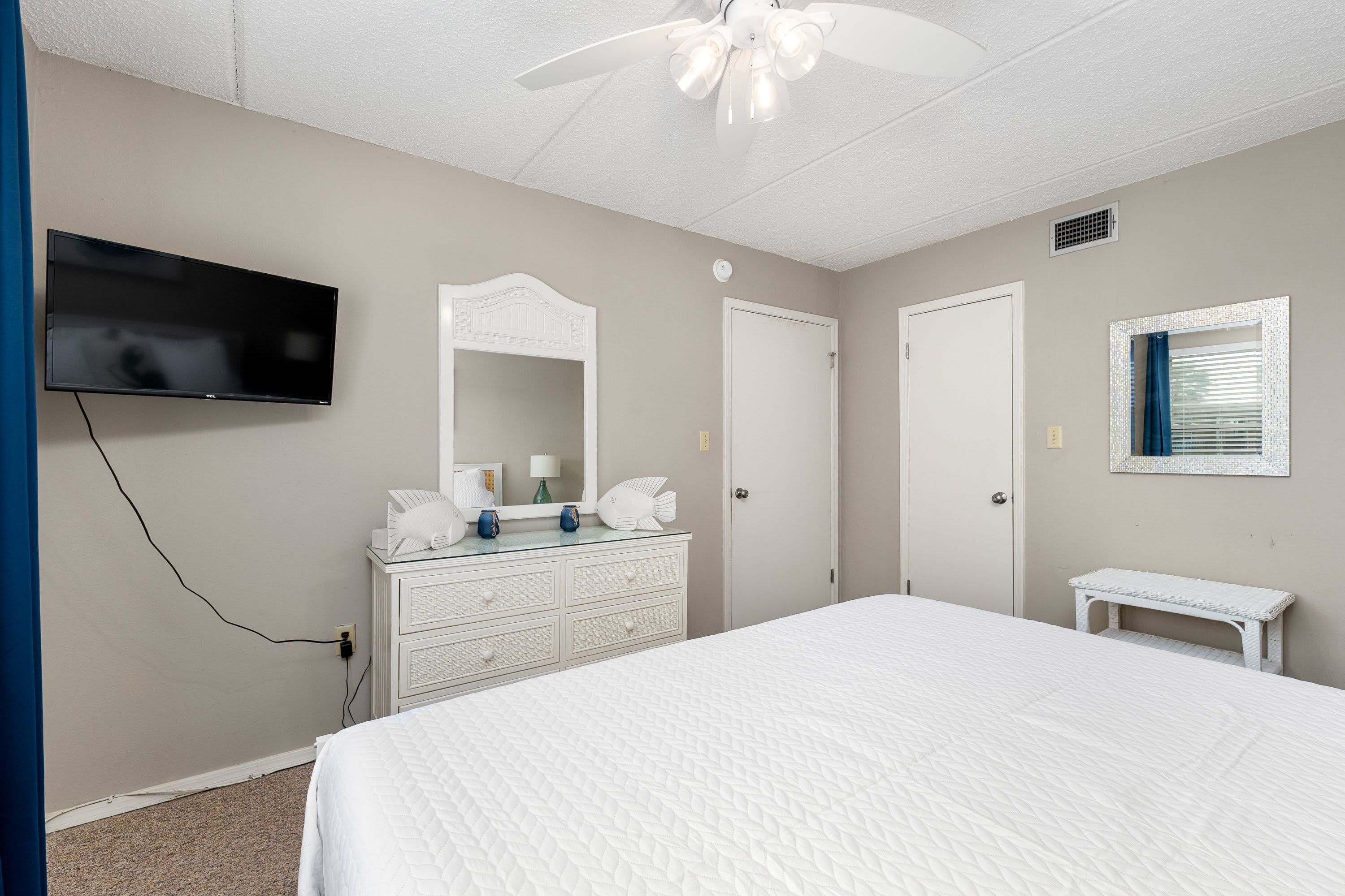 A bedroom with a bed, a dresser, a television, a ceiling fan, and a window with blinds.