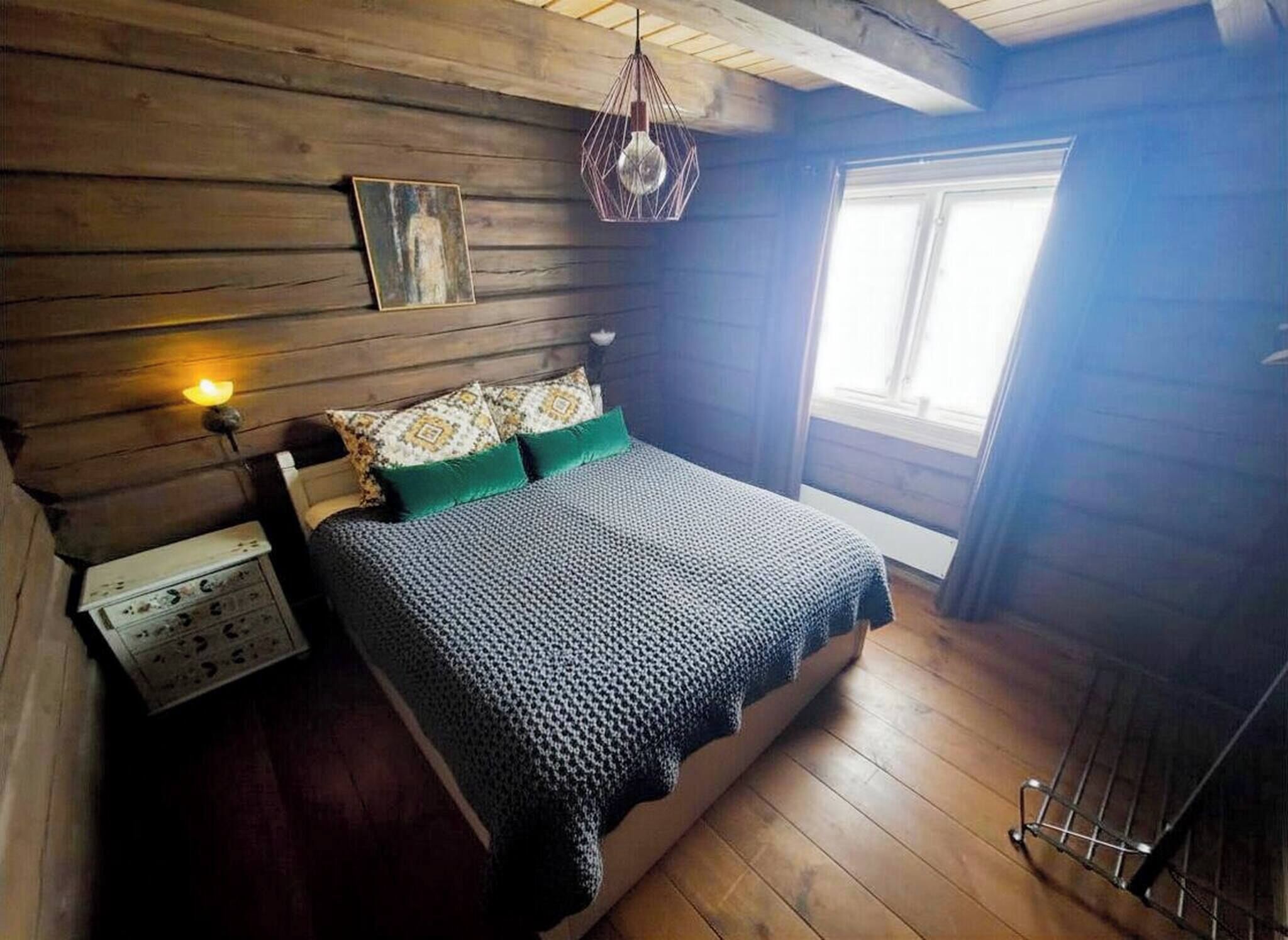 Une chambre confortable dans un chalet en rondins, avec un lit, une table de chevet, une lampe fixée au mur et une fenêtre.