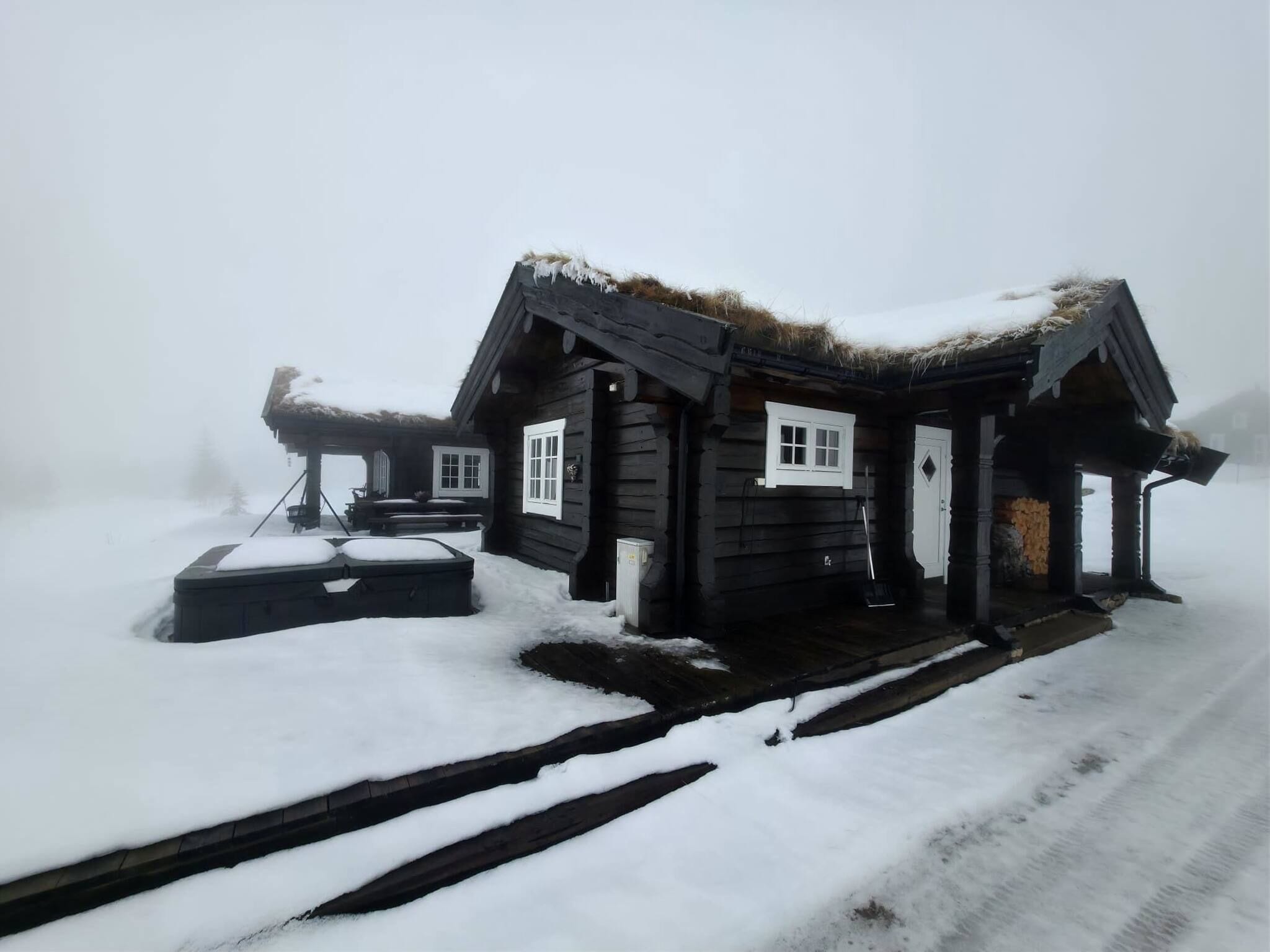 A log cabin with a thatched roof, a porch, and a snow-covered ground.