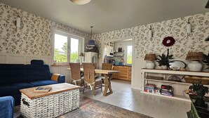 Un salon avec un canapé bleu, une table basse en osier et un coin repas comprenant une table et des chaises en bois.