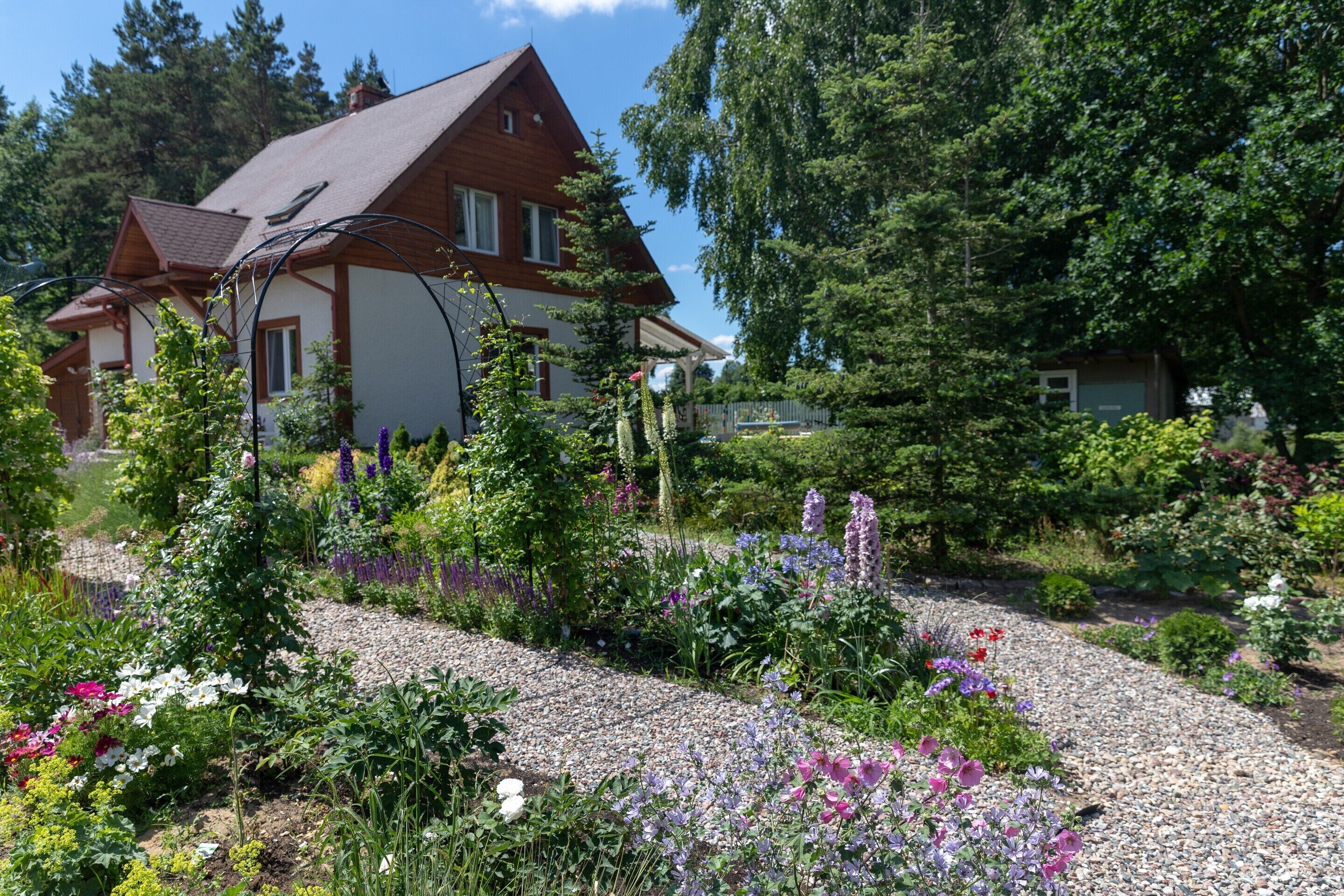 A house with a sloped roof, surrounded by a garden with various plants and flowers.