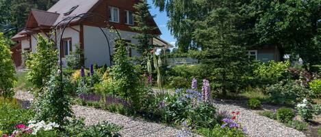 A house with a sloped roof, surrounded by a garden with various plants and flowers.