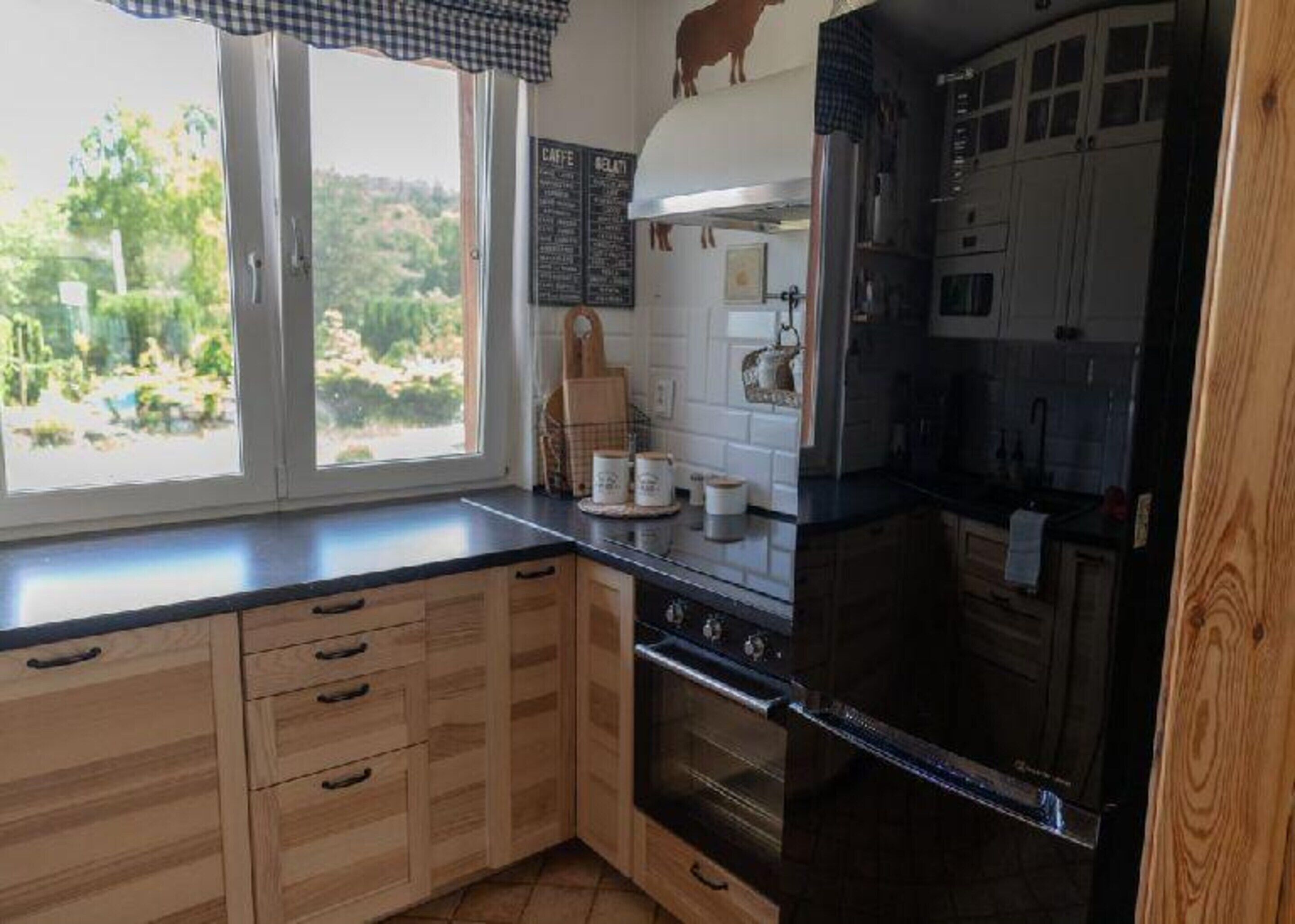 Eine Küche mit Holzausstattung, einem schwarzen Kühlschrank und einem Fenster mit Blick auf Grünflächen.