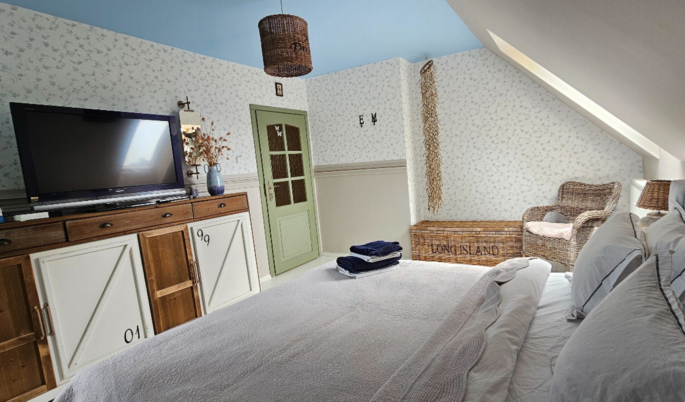 A bedroom with a bed, a television, a wicker chair, and a door with floral wallpaper.