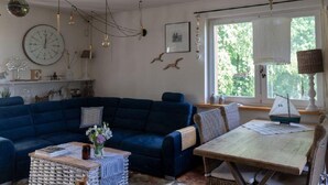 Un salon chaleureux avec un canapé bleu, une table à manger et une grande fenêtre agrémentée de rideaux.