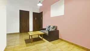 A room with a wooden floor, a sofa with patterned cushions, a small table, and two wooden doors. - Deluxe GL Classic (Alto de Porvorim)