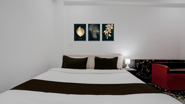 A hotel room with a bed, a nightstand, a red chair, and three wall-mounted artworks. - Deluxe Peepal Tree Bhagalpur (Bhāgalpur)