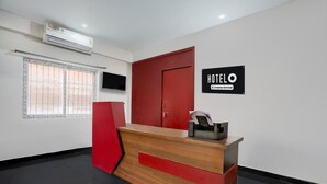 A hotel reception desk with a red and black color scheme, a mounted TV, and a window with blinds. - Deluxe Peepal Tree Bhagalpur (Bhāgalpur)