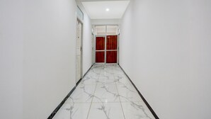 A hallway with a marble floor, white walls, and a red door at the end. - Deluxe Peepal Tree Bhagalpur (Bhāgalpur)