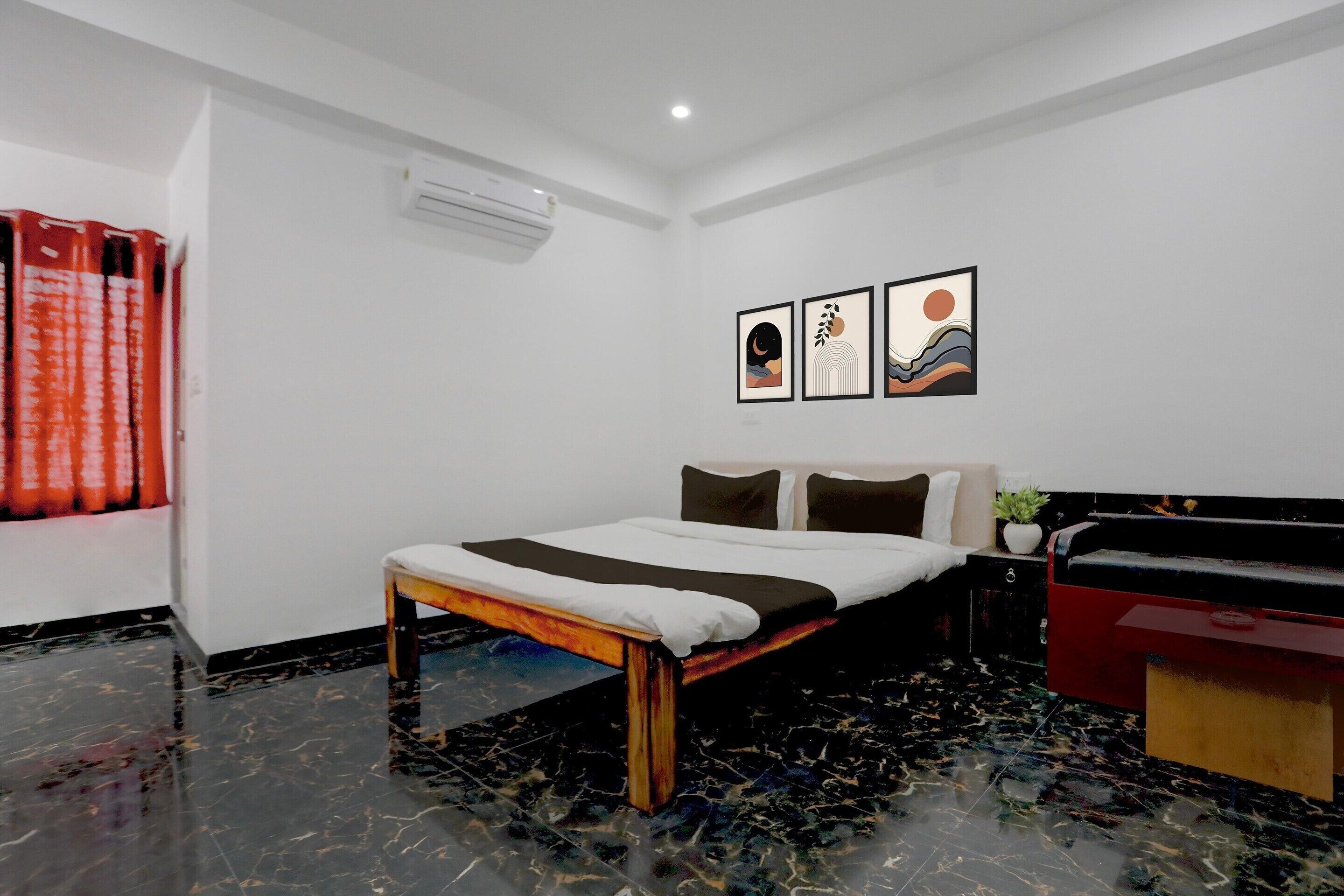 Habitación de hotel con cama, mesita de noche, cómoda roja y tres obras de arte enmarcadas en la pared.