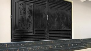 A black metal door with intricate floral designs, a white wall, and a marble staircase. - Deluxe Peepal Tree Bhagalpur (Bhāgalpur)