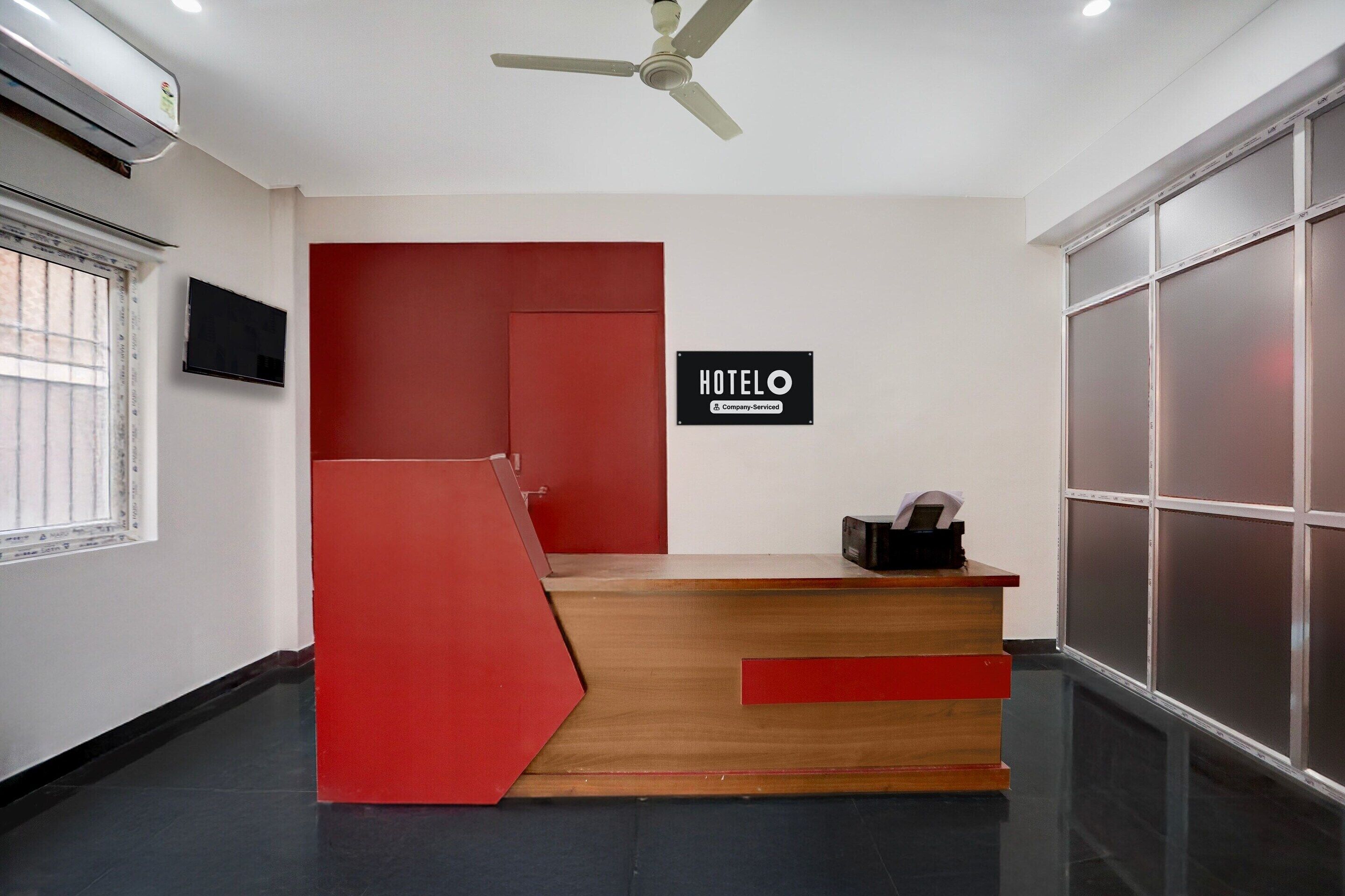 A hotel reception desk with a red and wooden design, a ceiling fan, and a sign that reads 'HOTELO.'