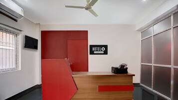A hotel reception desk with a red and wooden design, a ceiling fan, and a sign that reads 'HOTELO.'