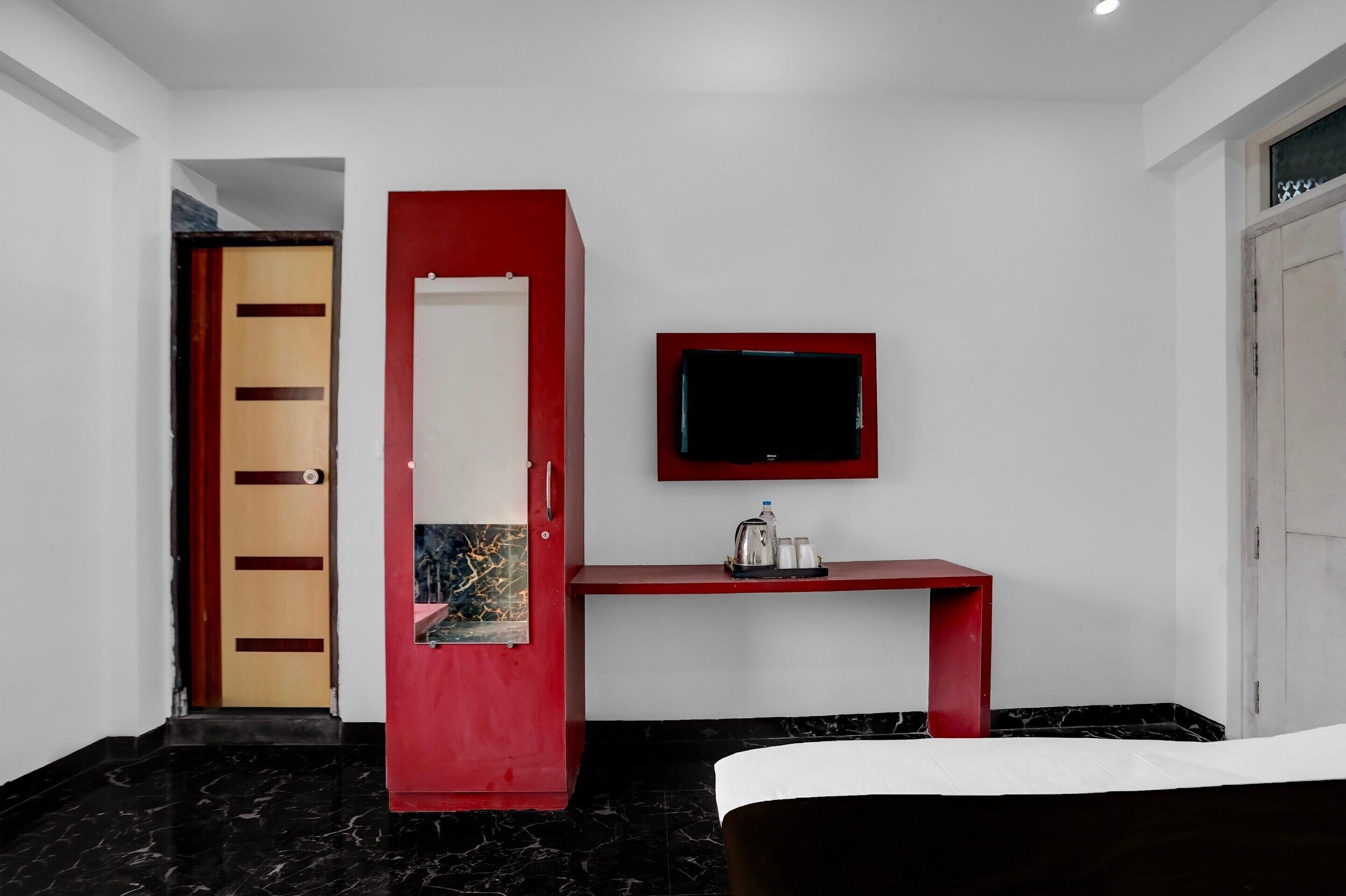 A hotel room with a bed, a red desk, a television, and a door.