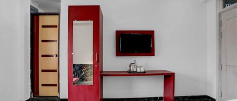 A hotel room with a bed, a red desk, a television, and a door.
