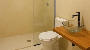 Un baño moderno con cabina de ducha de vidrio, inodoro blanco y tocador de madera con lavabo de vidrio.