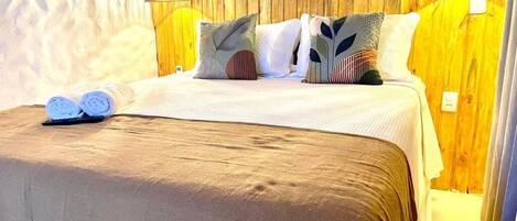 Una cama con una colcha marrón, dos almohadas y dos lámparas fijadas a la pared.