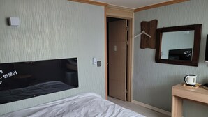 A hotel room with a bed, a bedside table with a kettle, a mirror, and a wardrobe.