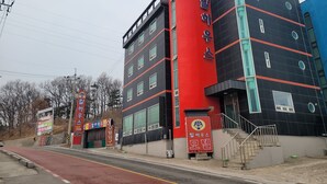 A multi-story building with a red and black facade, large windows, and a visible entrance with a staircase.