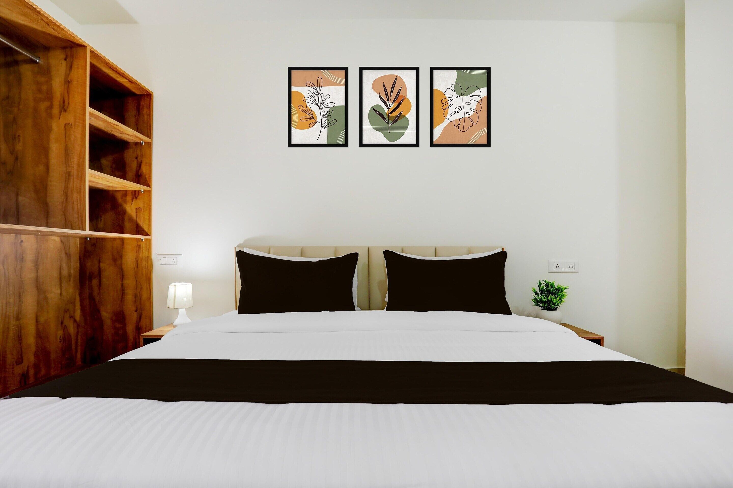 A bedroom with a bed, a wooden wardrobe, a nightstand with a lamp, and three framed artworks on the wall.