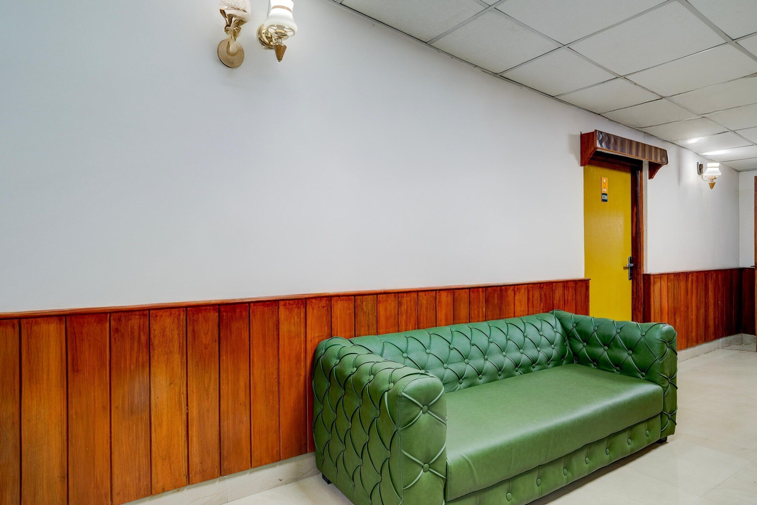 A green tufted sofa in a hallway with wooden paneling, a yellow door, and a white ceiling.