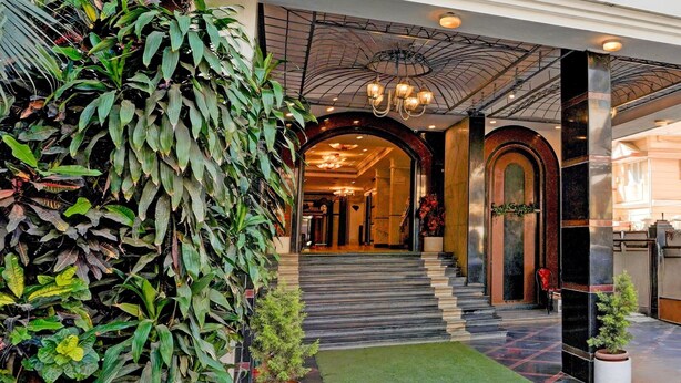 A hotel entrance with a staircase leading to the lobby, a large potted plant, and a chandelier. - Premiumhotel Seven Olive (Bengaluru)