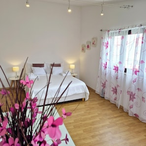 Une chambre à coucher comprenant un lit, des tables de chevet, une commode, une fenêtre avec des rideaux et un mur orné de tableaux.