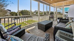 Un espacio al aire libre cubierto con mobiliario de mimbre, un ventilador de techo y ventanas amplias que ofrecen vistas del vecindario.