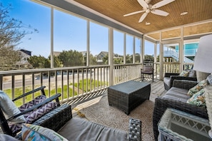 A covered outdoor area with wicker furniture, a ceiling fan, and large windows offering a view of the neighborhood. - Altman House 5 Bedroom Home (Pawleys Island)