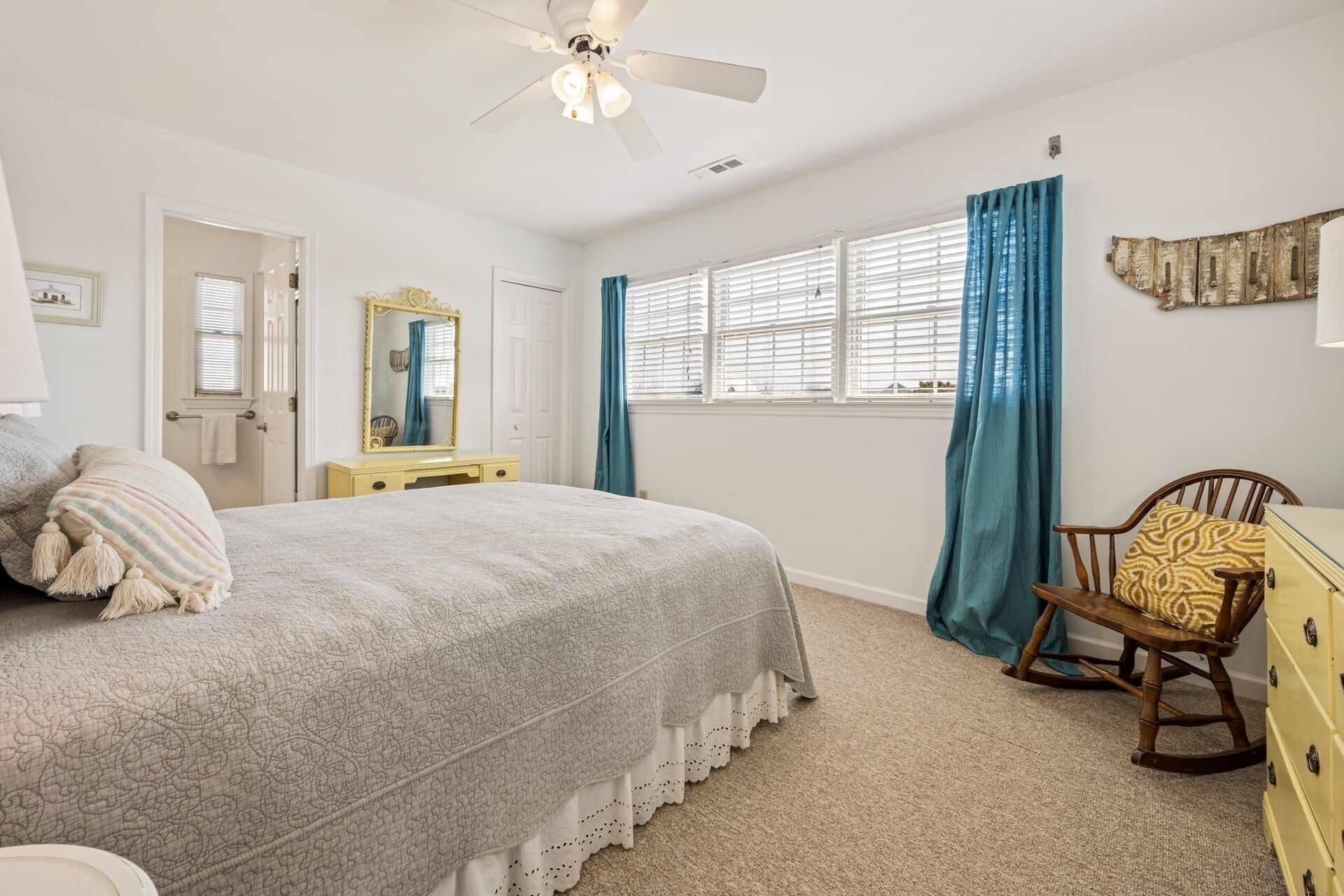 A bedroom with a bed, dresser, chair, and a window with curtains.