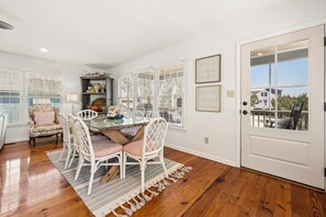A dining area with a glass table, white chairs, a rug, and a door leading outside. - Altman House 5 Bedroom Home (Pawleys Island)