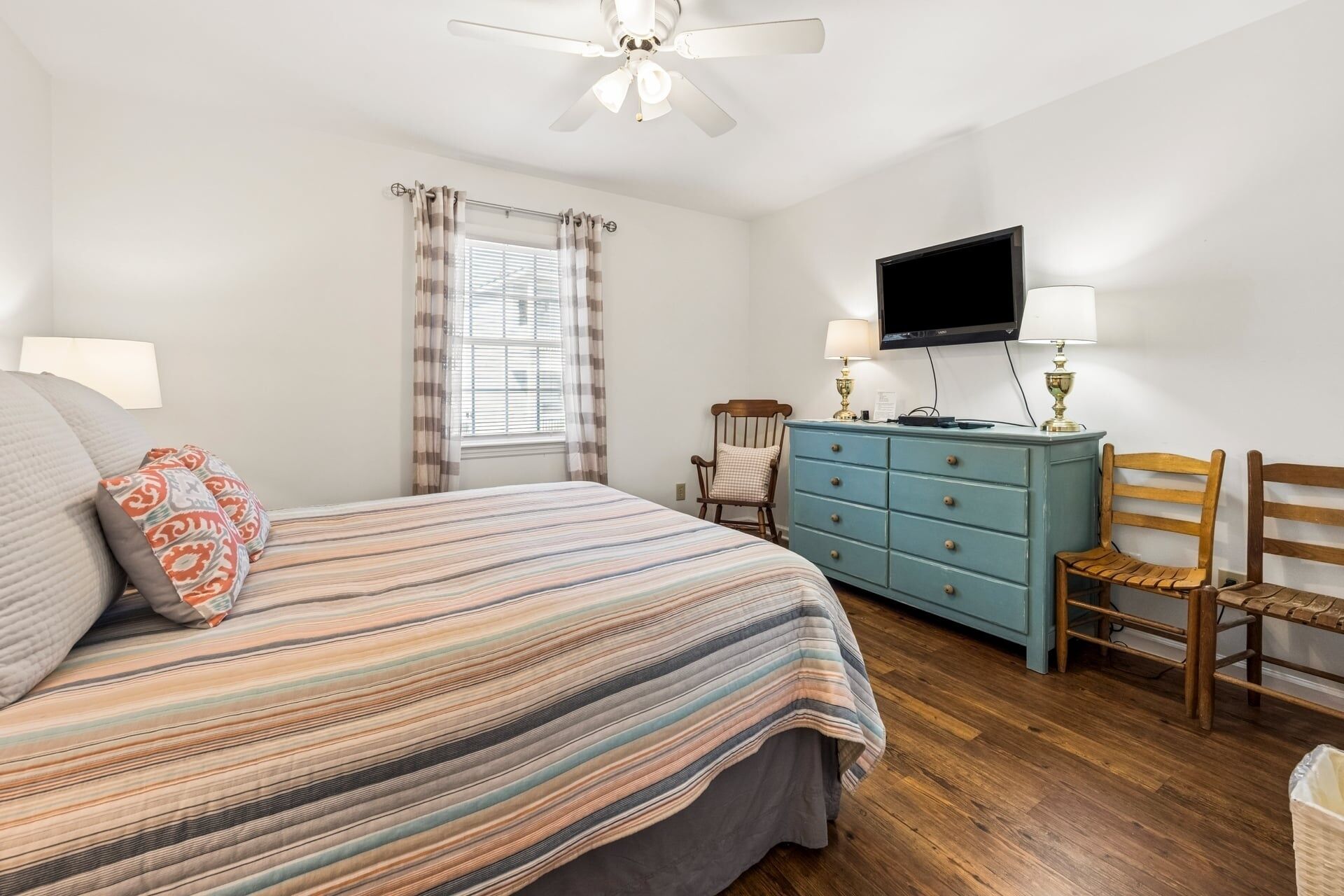 A bedroom with a bed, a dresser, a chair, a television, and a ceiling fan.
