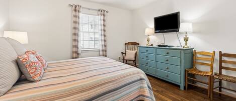 A bedroom with a bed, a dresser, a chair, a television, and a ceiling fan.