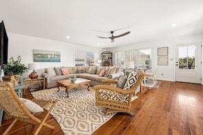 A spacious living room with a large sectional sofa, a coffee table, wicker chairs, and a ceiling fan. - Altman House 5 Bedroom Home (Pawleys Island)