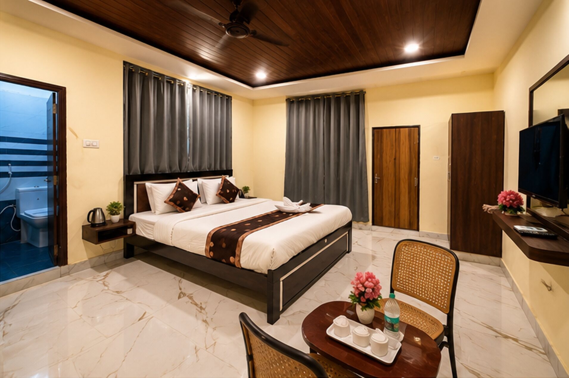 Habitación de hotel con cama, televisión, escritorio con ordenador, silla y mesita con una bandeja de objetos.