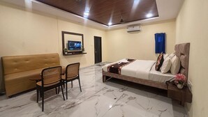 Ett hotellrum med en säng, en soffa, ett matbord med stolar, en TV och en takfläkt.
