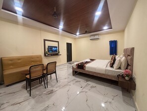 A hotel room with a bed, a sofa, a dining table with chairs, a TV, and a ceiling fan. - Hotel Sky Palace (Hyderabad)