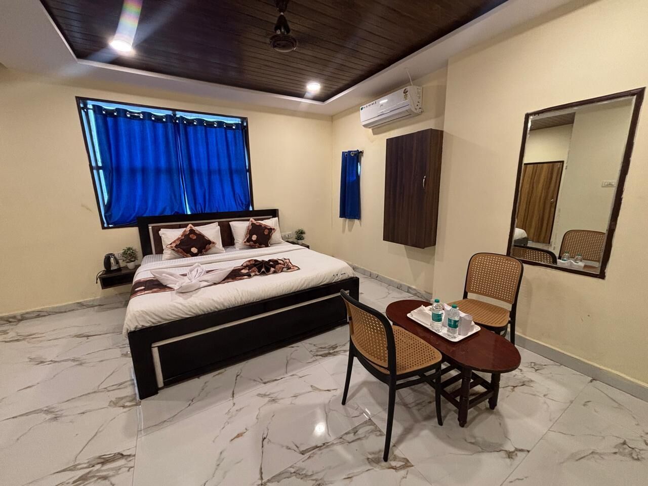 A bedroom with a bed, a table with chairs, a mirror, and an air conditioning unit.
