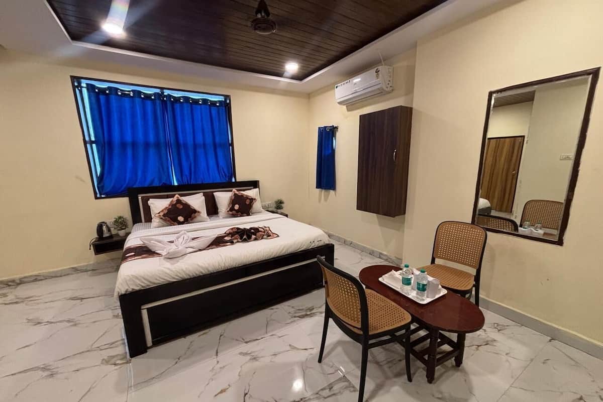 A bedroom with a bed, a table with chairs, a mirror, and an air conditioning unit.
