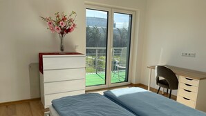 Un dormitorio con cama, escritorio, silla, cómoda y ventana con vista a follaje.