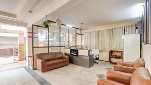 A reception area with a brown leather sofa, a reception desk, and a large mirror. - Super Collection O Kphb (Hyderabad)