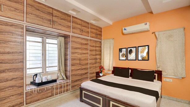 A bedroom with a bed, wardrobe, window, curtains, artwork, and an air conditioning unit. - Super Collection O Kphb (Hyderabad)