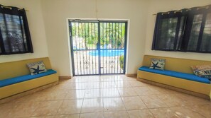A room with a sliding glass door leading to a pool area, two yellow sofas with blue cushions, and a tiled floor. - Quiet Tropimar stay, 2-bedroom condo with AC in vibrant Sosua (Sosua)
