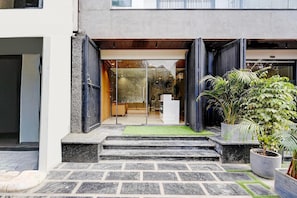 Entrada d'un edifici modern amb una porta de vidre, escales cap a una recepció i plantes en testos.