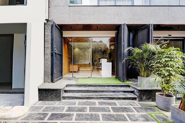 A modern building entrance with a glass door, steps leading up to a reception desk, and potted plants.