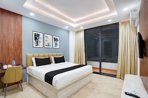 A hotel room with a bed, desk, chair, artwork, and a sliding glass door to the outside.