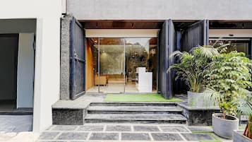 A modern building entrance with a glass door, steps leading up to a reception desk, and potted plants.