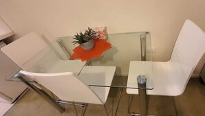 Een tafeltje met glazen blad, twee witte stoelen, een bloempot en een klein oranje decoratie.