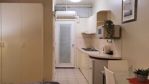 Een smalle gang die leidt naar een keuken met een koelkast, gootsteen en een kleine eethoek.